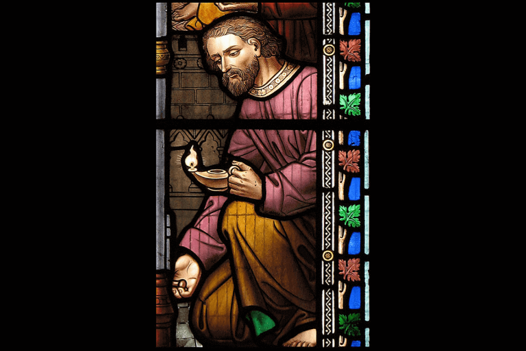 Stained glass artwork of a man with brown hair and a beard huddled over a barrel and holding a burning oil lamp.