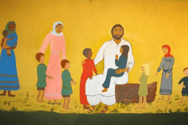 A folk art–style mural on a yellow background depicting Jesus seated on a wooden stump, holding a child on his lap while surrounded by a diverse group of women and children of various ethnicities. The figures wear simple, colorful robes in shades of blue, pink, red, and gray. The scene evokes the biblical passage "Let the little children come to me" (Matthew 19:14).