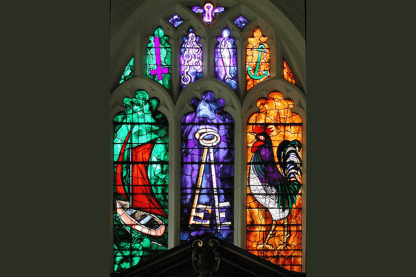 A stained glass mural with a purple pane in the middle, featuring two golden keys on it. On the right, there is a golden pane with a rooster on top. To the left, there is a green pane with a sailboat, featuring a red sail.